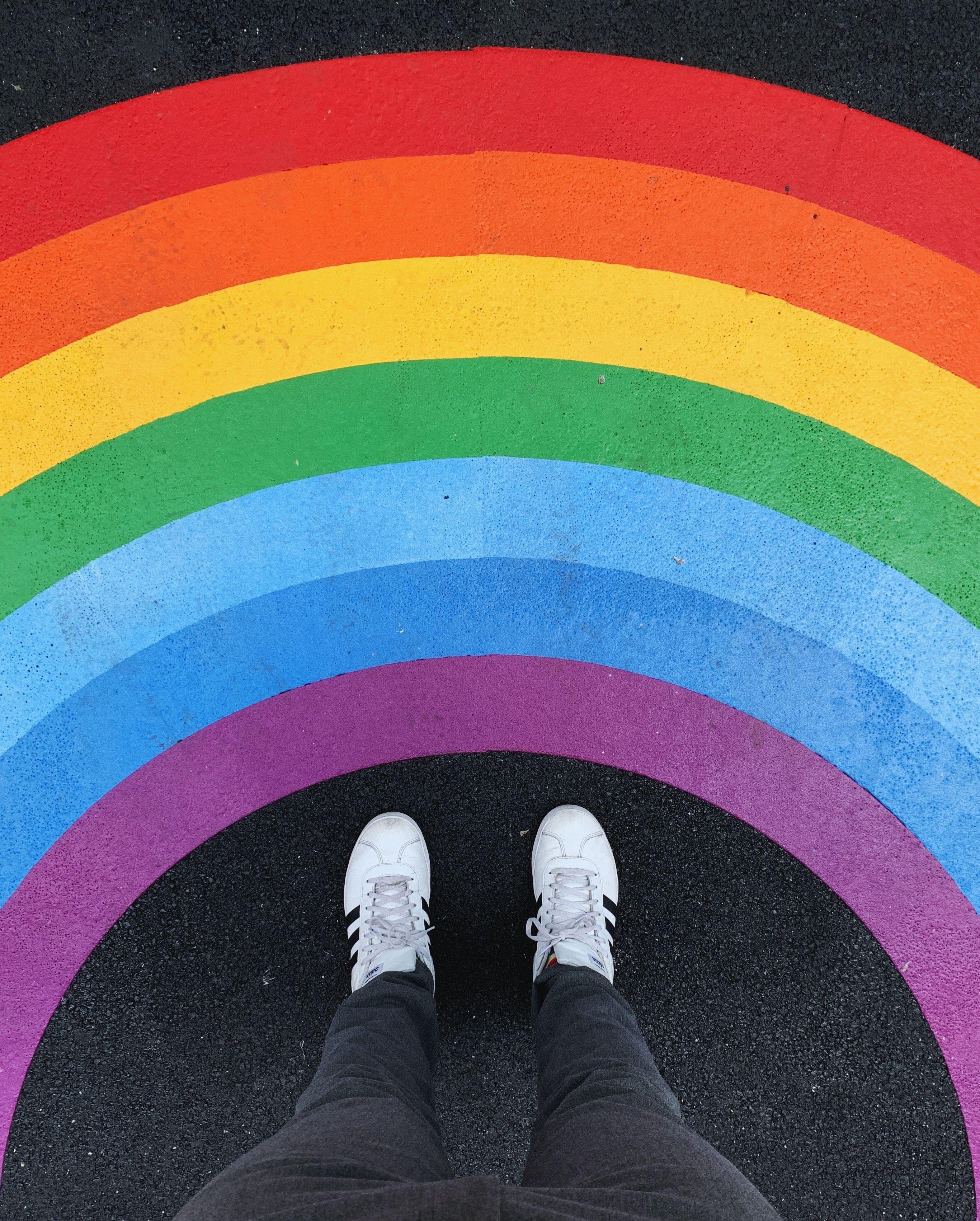 Feet in white sneakers standing under the centre of a rainbow 